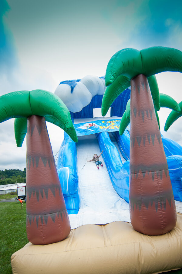 A child sliding down a giant inflatable slide that looks like a tidal wave with palm trees
