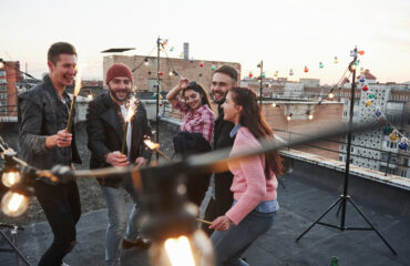 Happy holidays. Playing with sparklers on the rooftop. Group of young beautiful friends